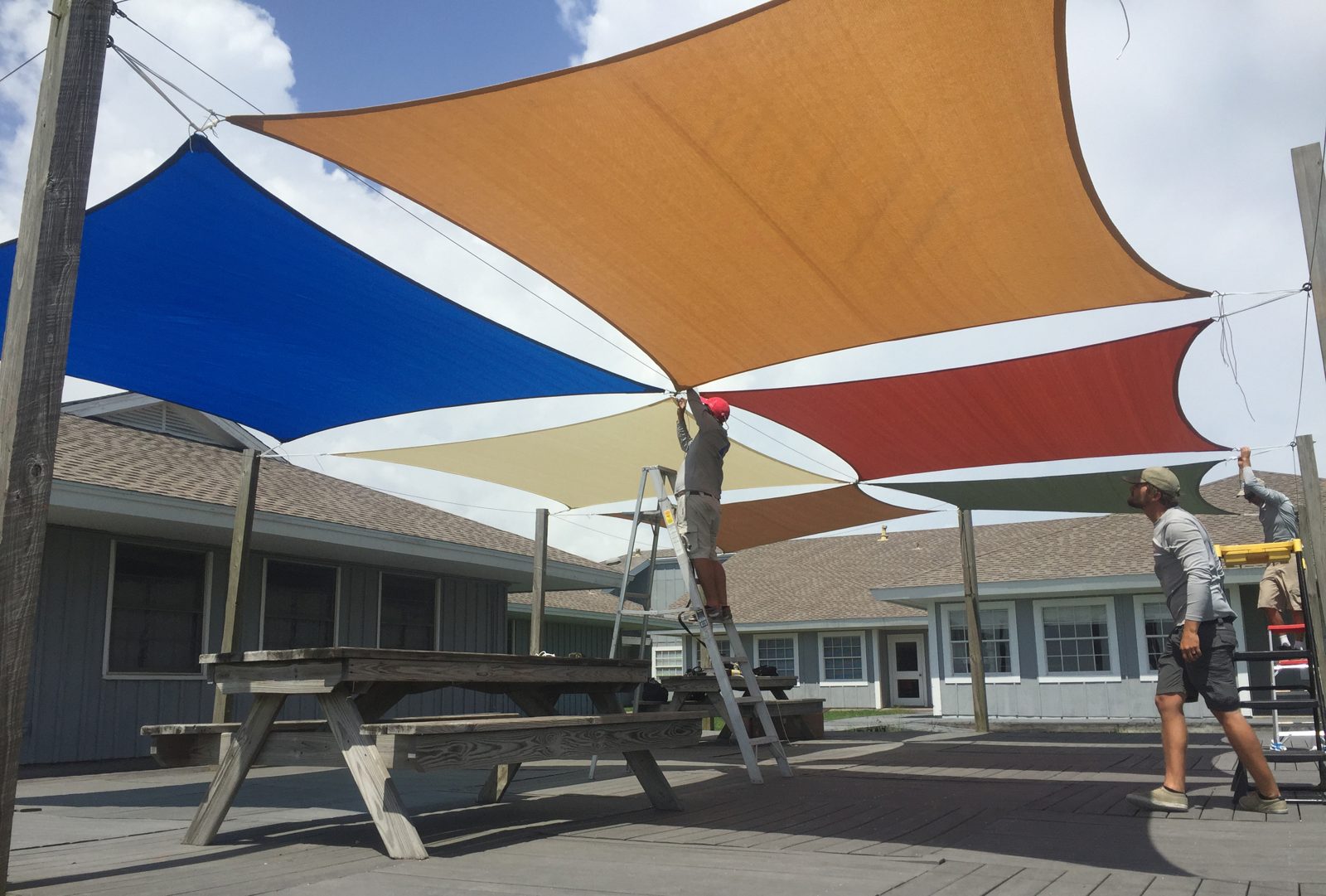Overlapping square sails being installed over a patio